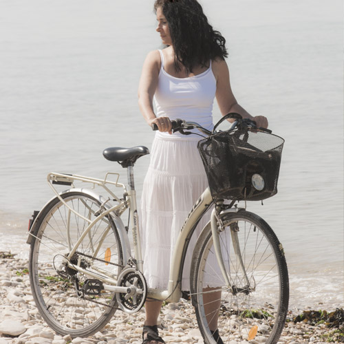 Foto de la artista Mayka Kaíma con su bici en la playa  vestida de blanco